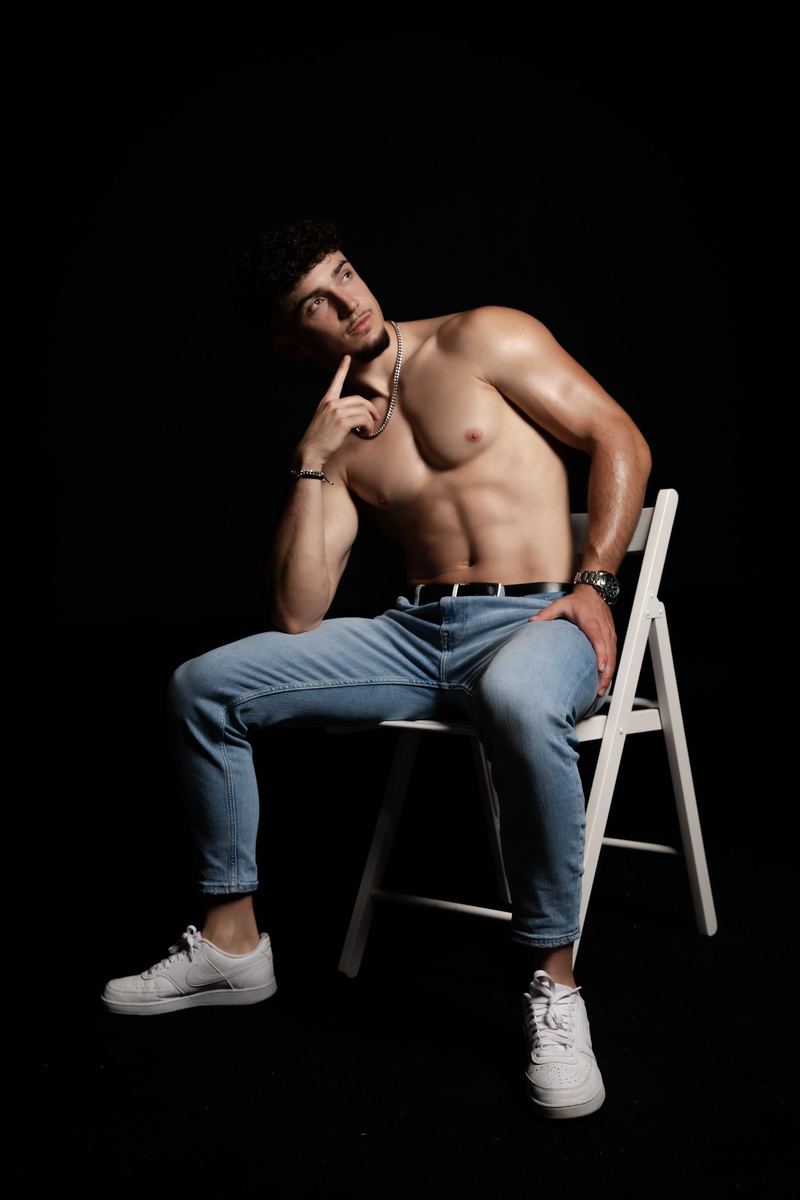 Mann mit freiem Oberkörper sitzt in Jeans auf einem Stuhl