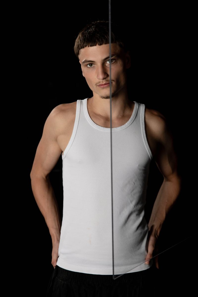 Junger Mann im weissen Tanktop, eine Glaskante teilt das Bild senkrecht