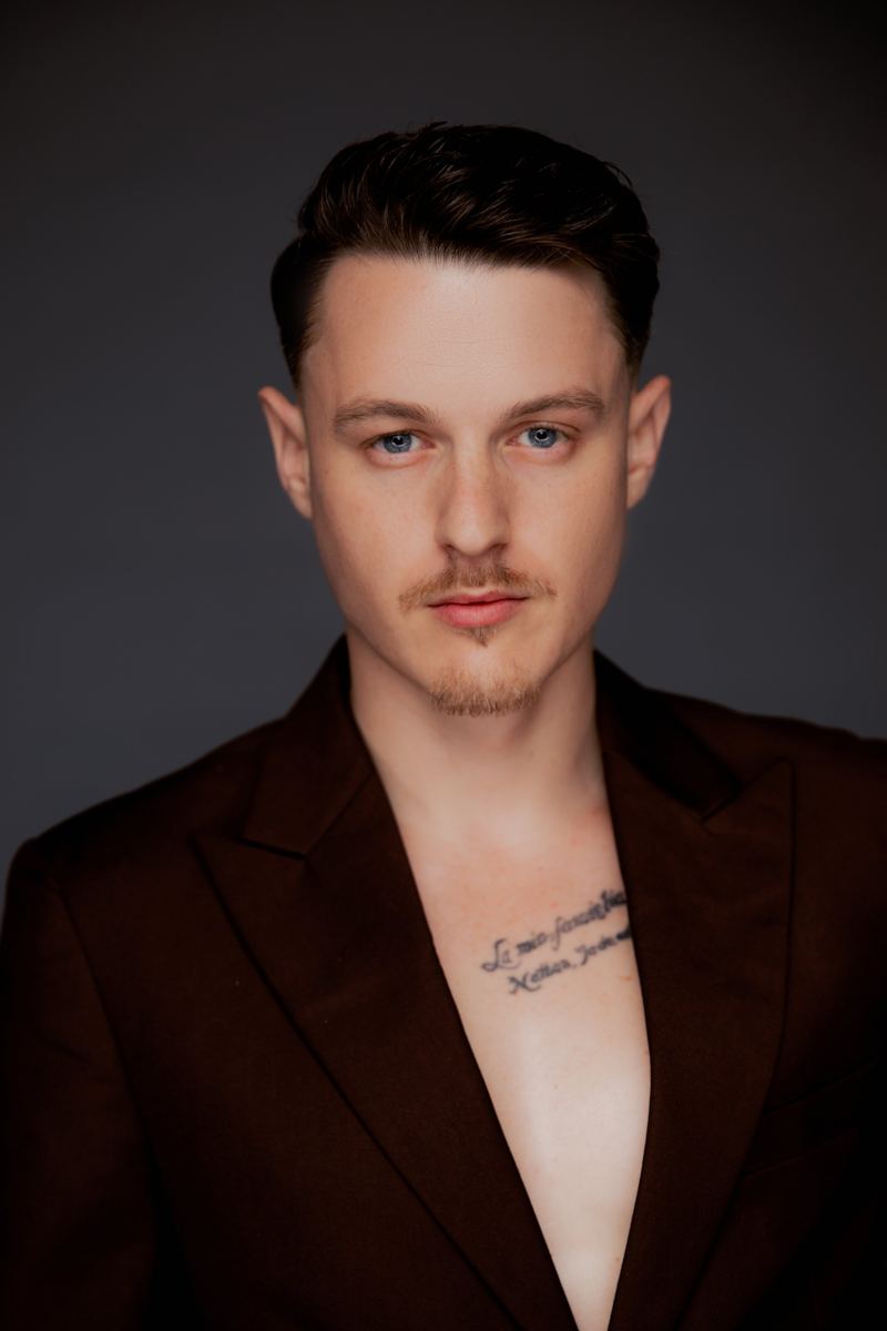 Mann im Sakko mit offenem Kragen, Tattoo auf der Brust