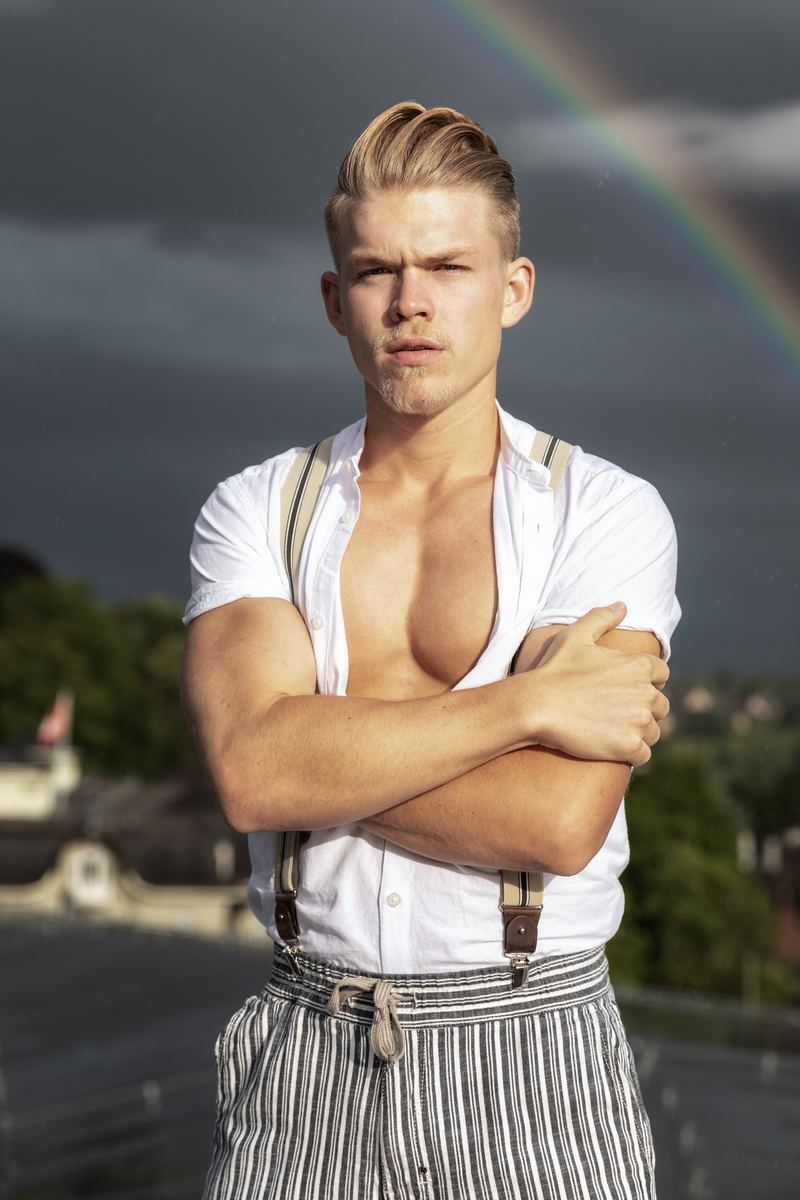 Mann mit Hosenträgern auf einem Dach, im Hintergrund ein Regenbogen