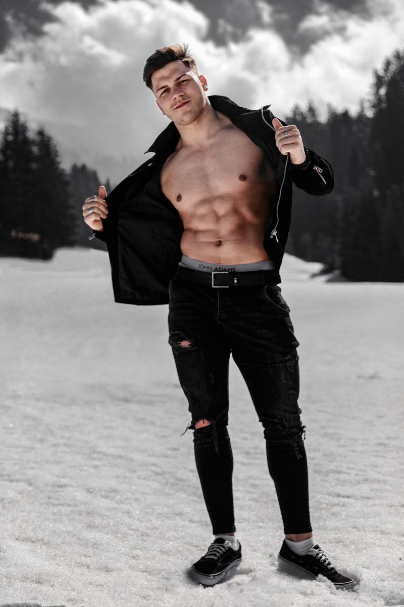 Mann öffnet seine Jacke in einer Schneelandschaft