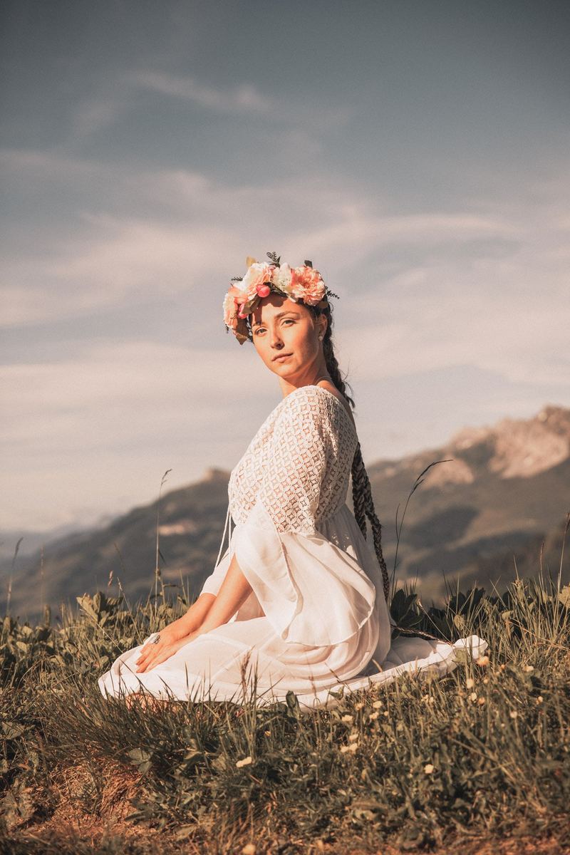 Frau mit Blumenkranz im Kleid auf einer Bergwiese