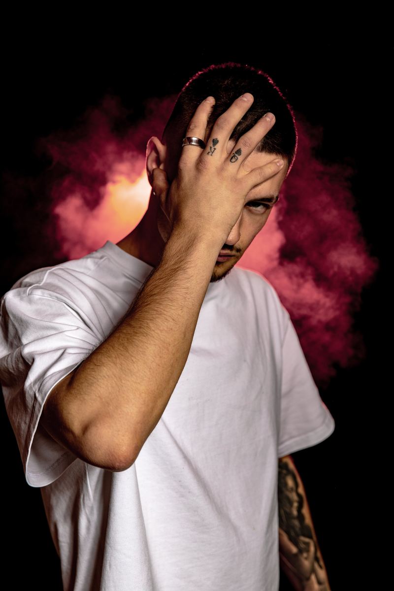 Mann im T-Shirt, Hand am Kopf, Rauch im Hintergrund